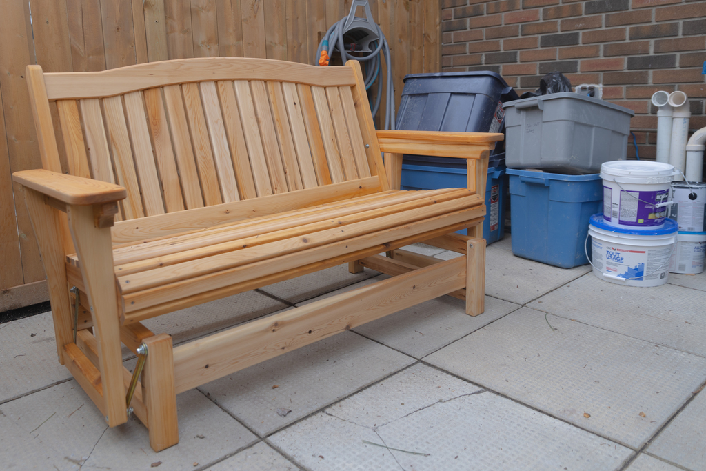 Premium handcrafted 3-seater cedar fanback glider bench featuring a contoured backrest on a backyard patio.