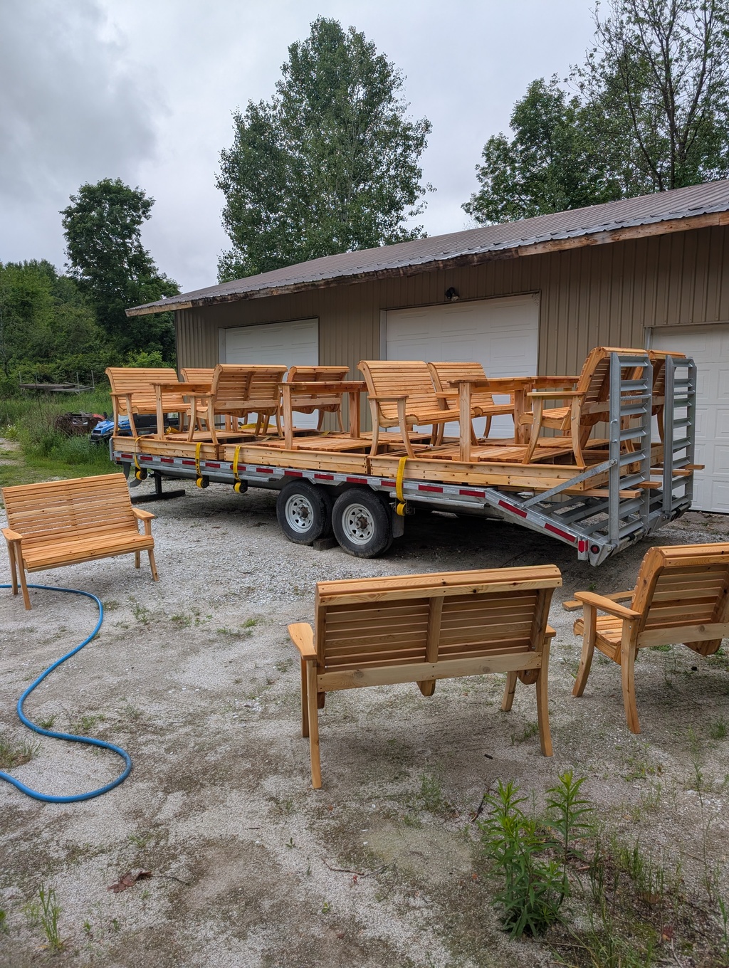 Multiple custom-built 4-person wooden glider sets loaded and strapped down onto a flatbed transport trailer for delivery outside a workshop.
